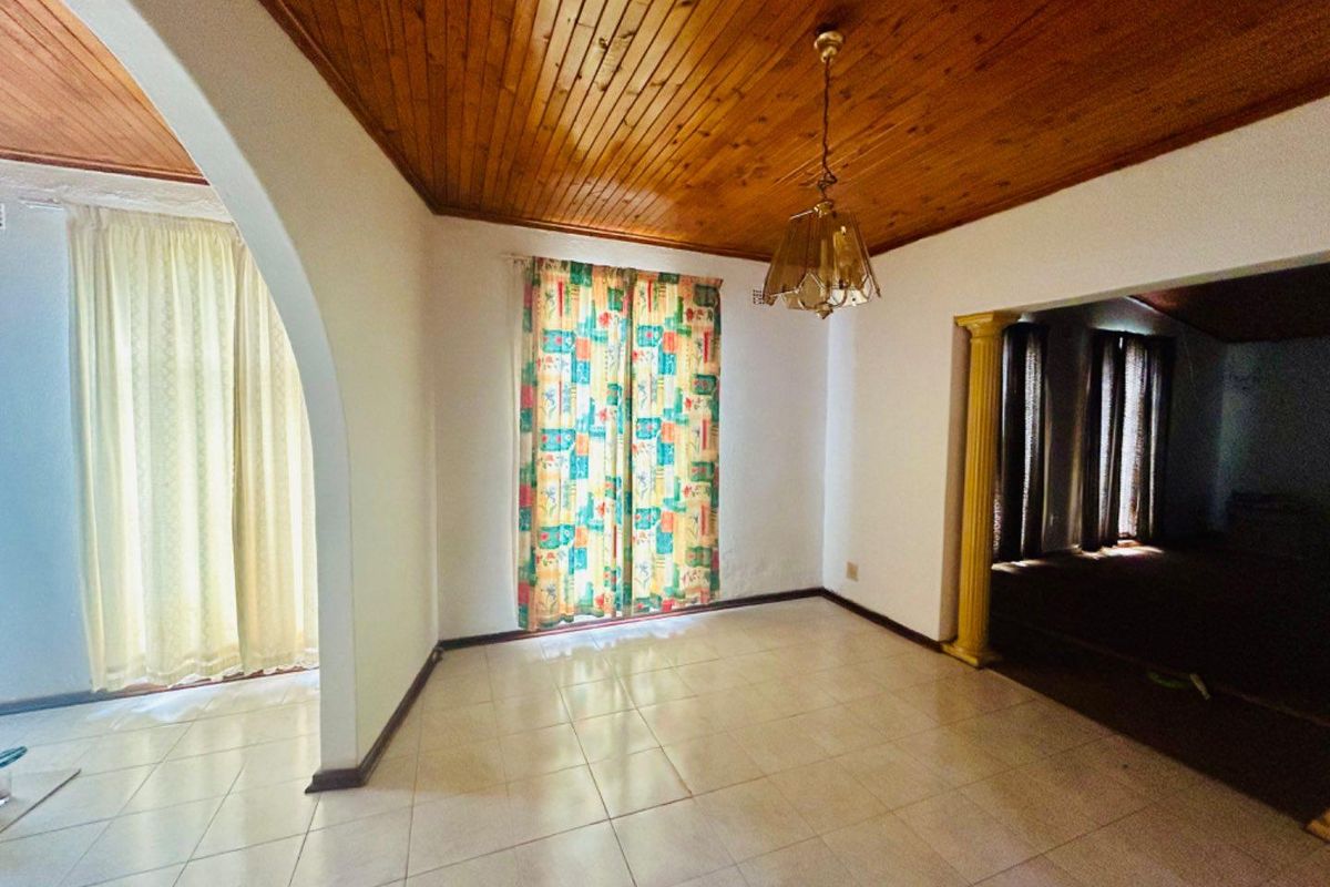 A bright living area featuring tiled flooring, a timber-paneled ceiling, and an arched entryway leading to an adjacent space.