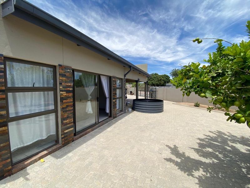 Rear exterior view featuring a paved patio area, sliding glass doors, stone-clad accents, and a metal water tank set against a boundary wall.