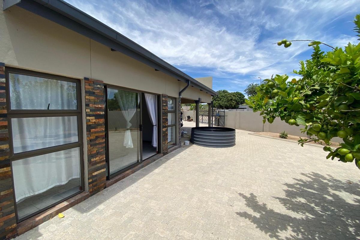 Rear exterior view featuring a paved patio area, sliding glass doors, stone-clad accents, and a metal water tank set against a boundary wall.