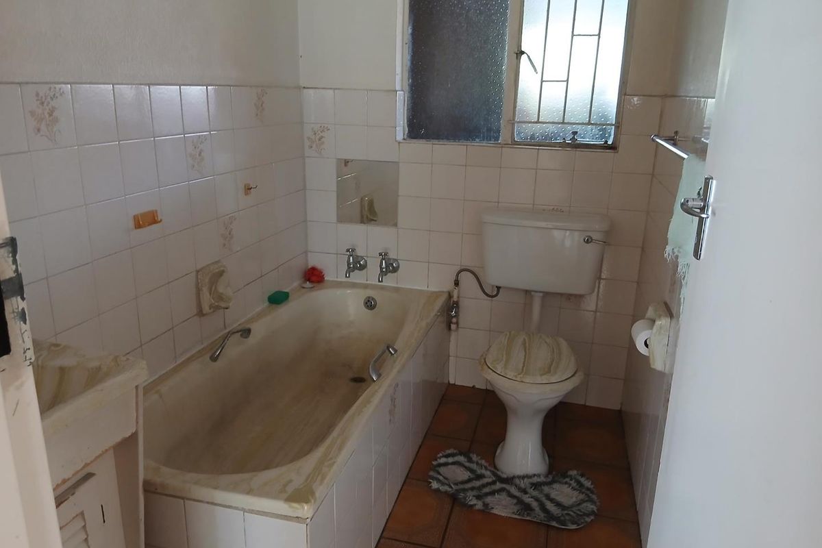A dated bathroom featuring a built-in bathtub, standard toilet, and tiled walls. The space requires modernization and refurbishment of fixed finishes.