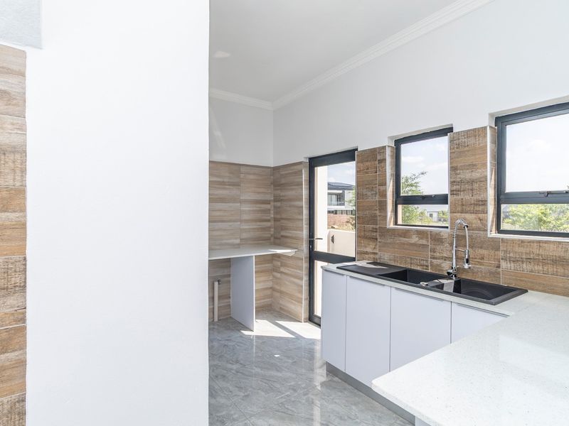 Modern kitchen featuring sleek white cabinetry, stone countertops, a double sink with a gooseneck faucet, and stylish wood-look tiled splashbacks.