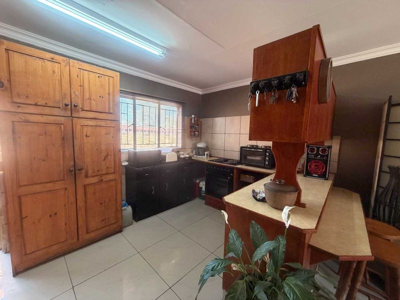 A functional kitchen featuring tiled flooring, a tiled backsplash, and built-in wooden cabinetry with a freestanding stove and ample storage space.