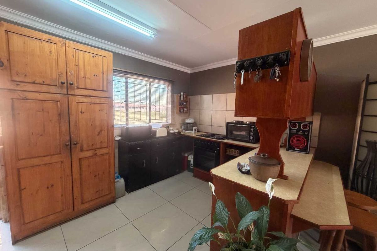 A functional kitchen featuring tiled flooring, a tiled backsplash, and built-in wooden cabinetry with a freestanding stove and ample storage space.