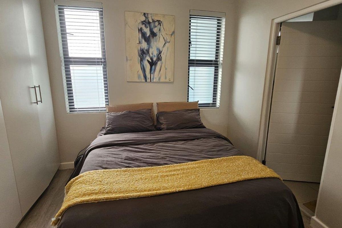 A well-maintained bedroom featuring built-in cupboards, laminate flooring, and dual windows with venetian blinds, providing a clean and functional living space.