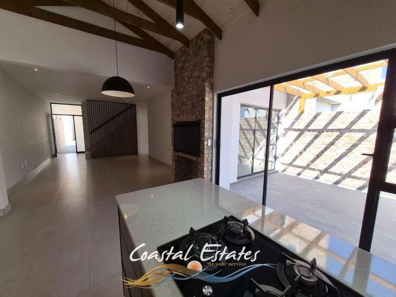 Spacious open-plan living area featuring exposed timber beams, a brick fireplace, and a modern kitchen island with gas hob, opening onto a covered patio.