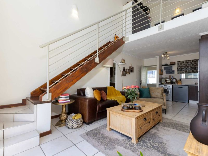 Open-plan living area featuring a staircase to a mezzanine level, tiled flooring, and an integrated kitchen and laundry space.