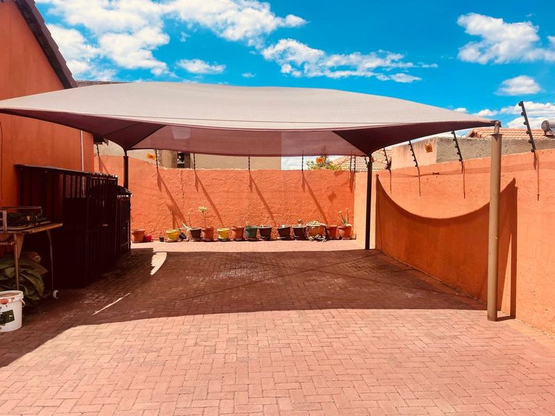 A paved outdoor patio area featuring a large shade sail, enclosed by perimeter walls with integrated electric fencing.