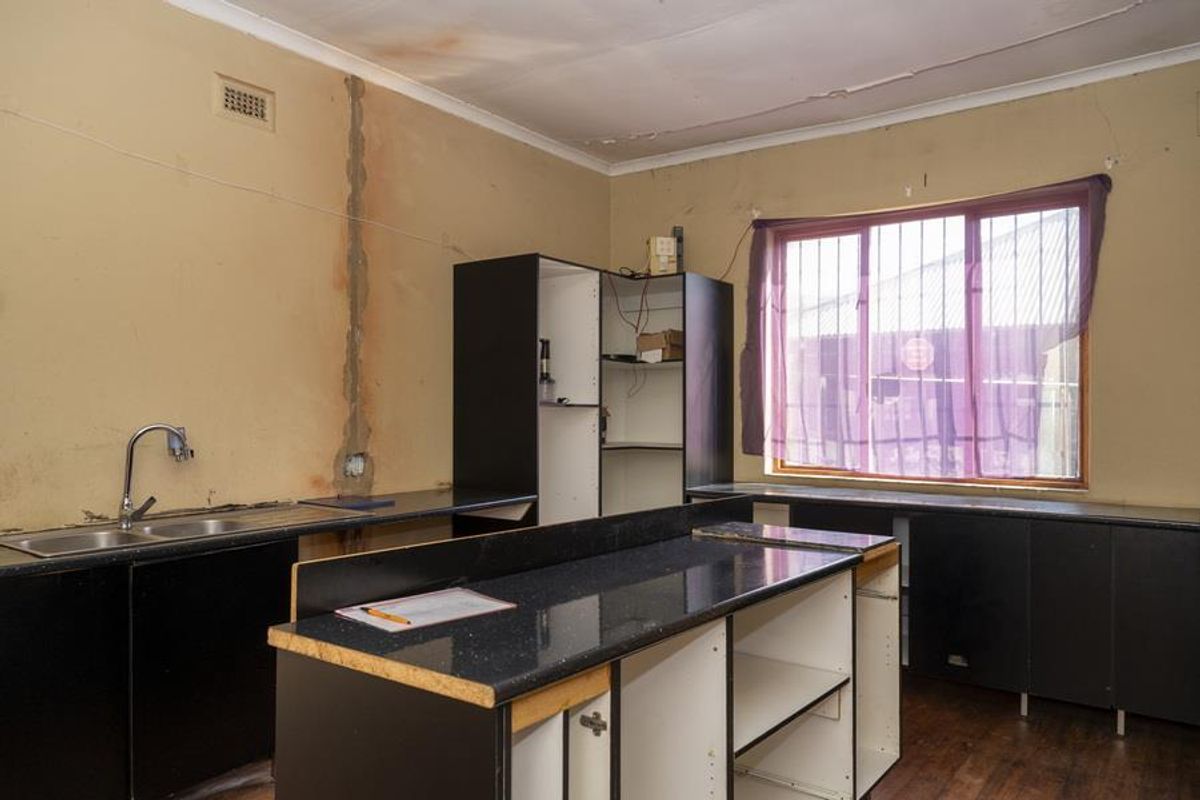 A dated kitchen space featuring black cabinetry, a double sink, and significant signs of wear including ceiling water damage and wall plaster deterioration.