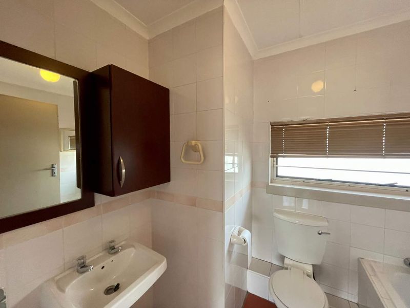 A functional bathroom featuring a wall-mounted basin, toilet, and wall-mounted storage cabinet with neutral tiled walls and a window for natural light.