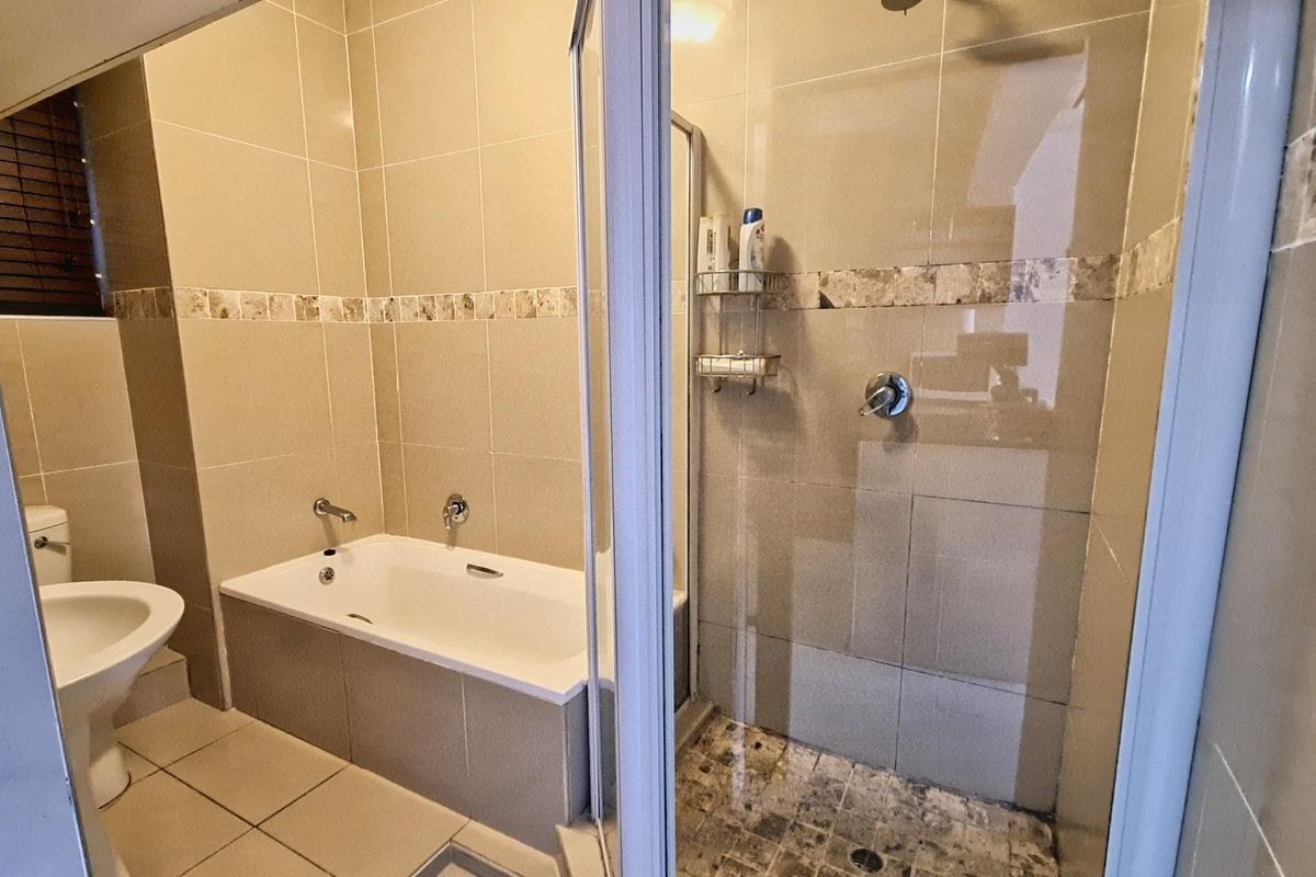 A functional bathroom featuring a built-in bathtub, a separate shower enclosure with glass door, and neutral ceramic tiling throughout.