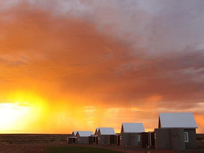 A scenic view of modern farm-style dwellings with corrugated metal roofs set against a dramatic sunset sky.