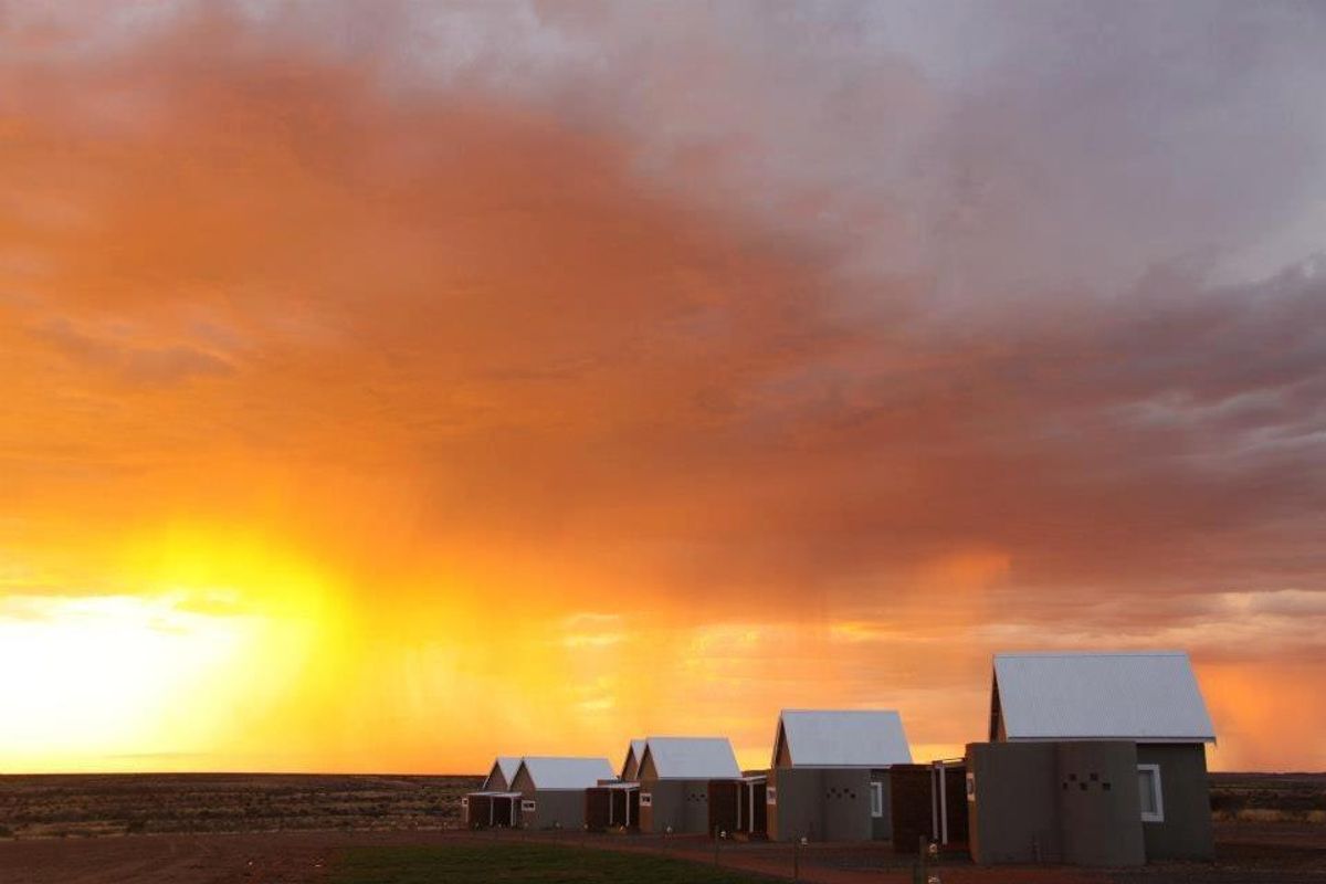 A scenic view of modern farm-style dwellings with corrugated metal roofs set against a dramatic sunset sky.