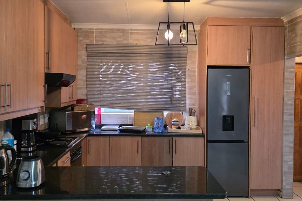 A functional kitchen featuring light wood cabinetry, dark granite countertops, tiled backsplash, and a breakfast bar area.