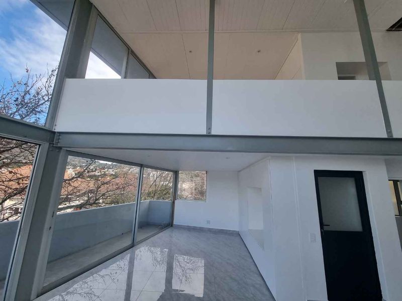 Spacious double-volume living area featuring floor-to-ceiling glass walls, modern tiled flooring, and an open mezzanine level with contemporary steel structural elements.
