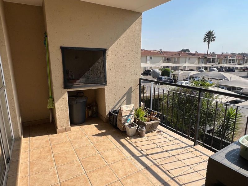 A covered balcony featuring tiled flooring, a built-in braai, and a metal balustrade, offering an outdoor space for relaxation.