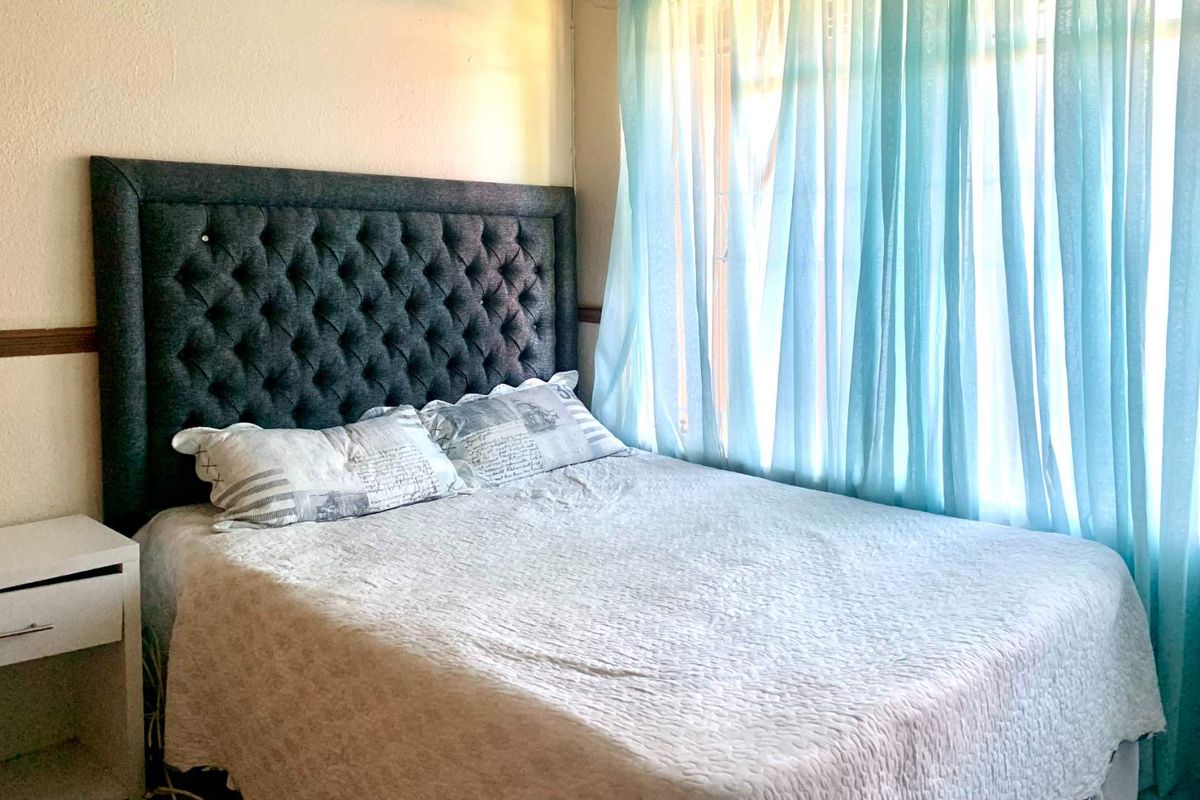 A bedroom featuring a window with light blue curtains and a neutral wall finish.