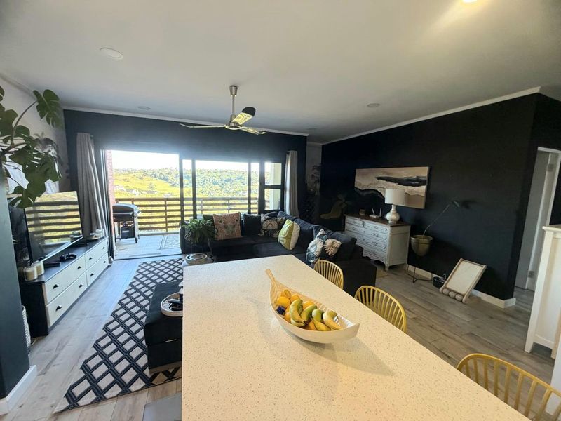 Spacious open-plan living area featuring modern laminate flooring, recessed lighting, a ceiling fan, and large sliding doors leading to a balcony with scenic views.