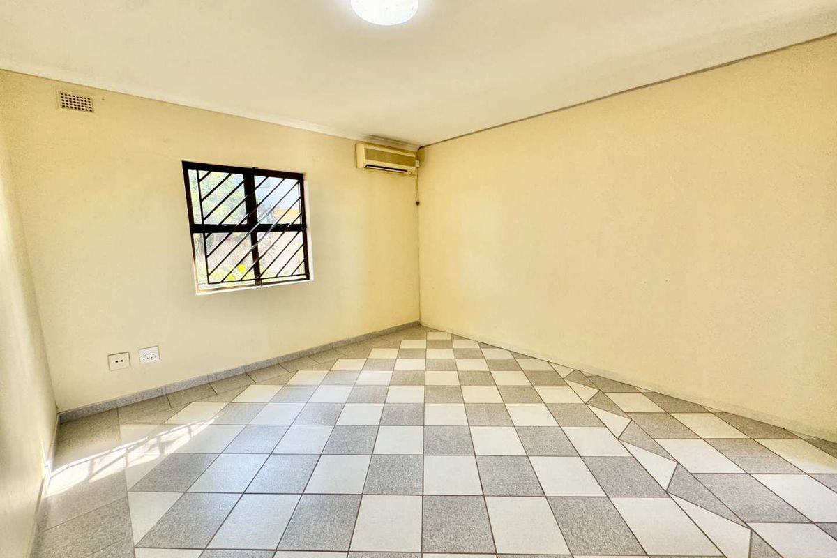 A vacant bedroom featuring tiled flooring, a wall-mounted air conditioning unit, and a window with security bars.