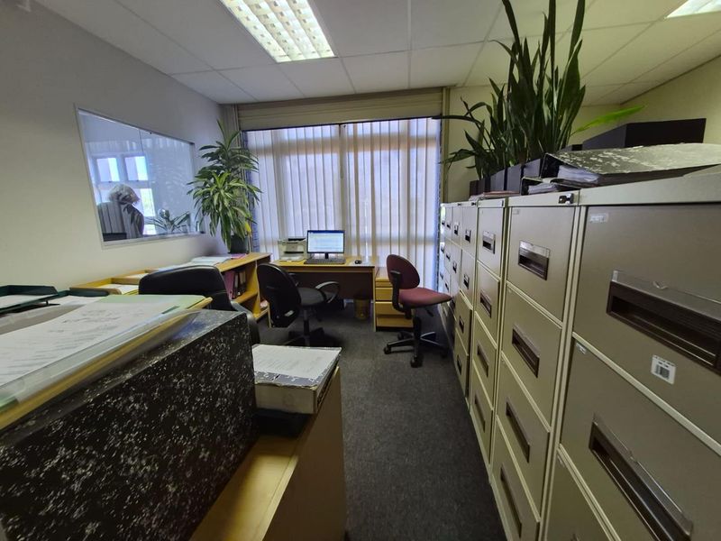 A functional office space featuring carpeted flooring, suspended ceiling lighting, and vertical blinds, providing a practical work environment.