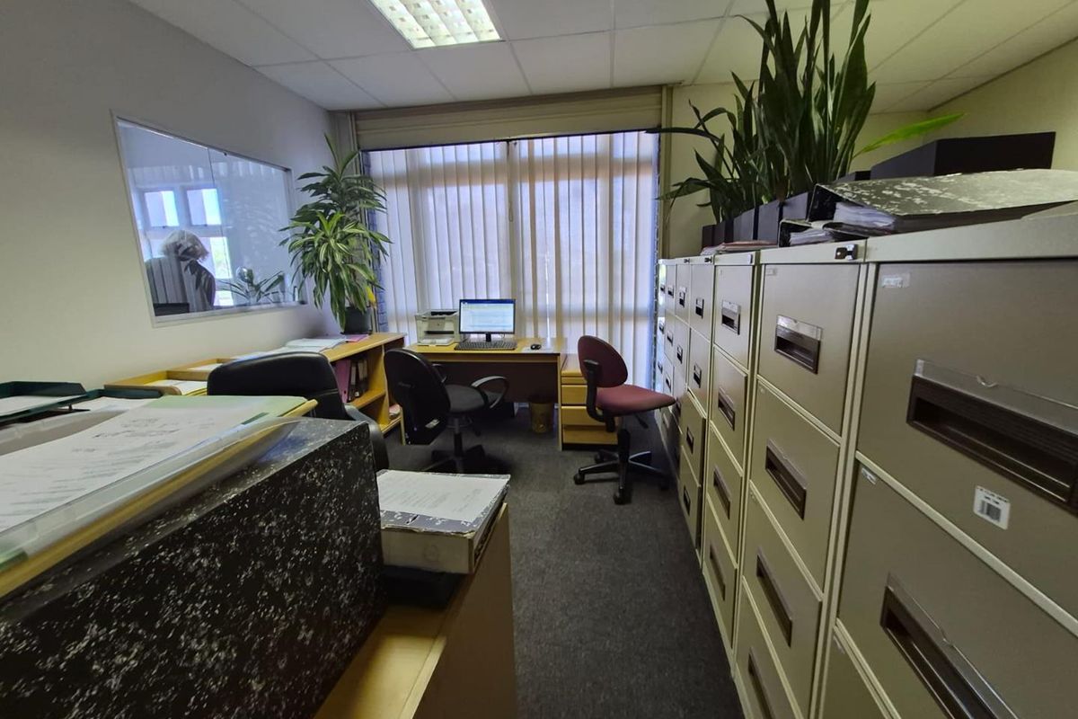 A functional office space featuring carpeted flooring, suspended ceiling lighting, and vertical blinds, providing a practical work environment.