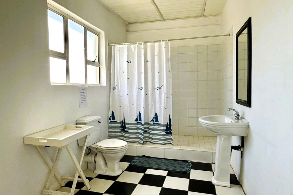 A functional bathroom featuring a pedestal basin, a shower with a tiled base, and a classic black and white checkered floor.
