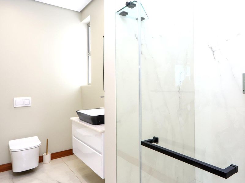 Modern bathroom featuring a wall-hung toilet, sleek vanity with vessel sink, and a spacious glass-enclosed shower with marble-look wall tiles.