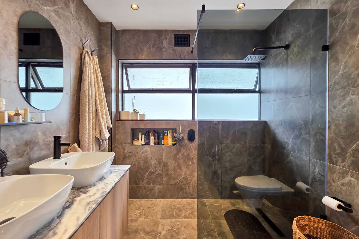 Modern bathroom featuring a double vanity with vessel sinks, a spacious walk-in shower with a rain shower head, and elegant marble-look tiling throughout.