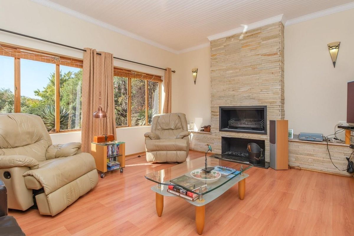 A bright living room featuring a prominent stone-clad fireplace, laminate flooring, and large timber-framed windows that provide natural light and garden views.