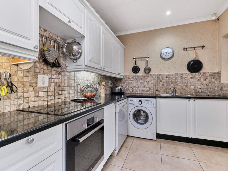 A functional kitchen featuring white cabinetry, granite countertops, a mosaic tile backsplash, built-in oven, and integrated laundry appliance space.