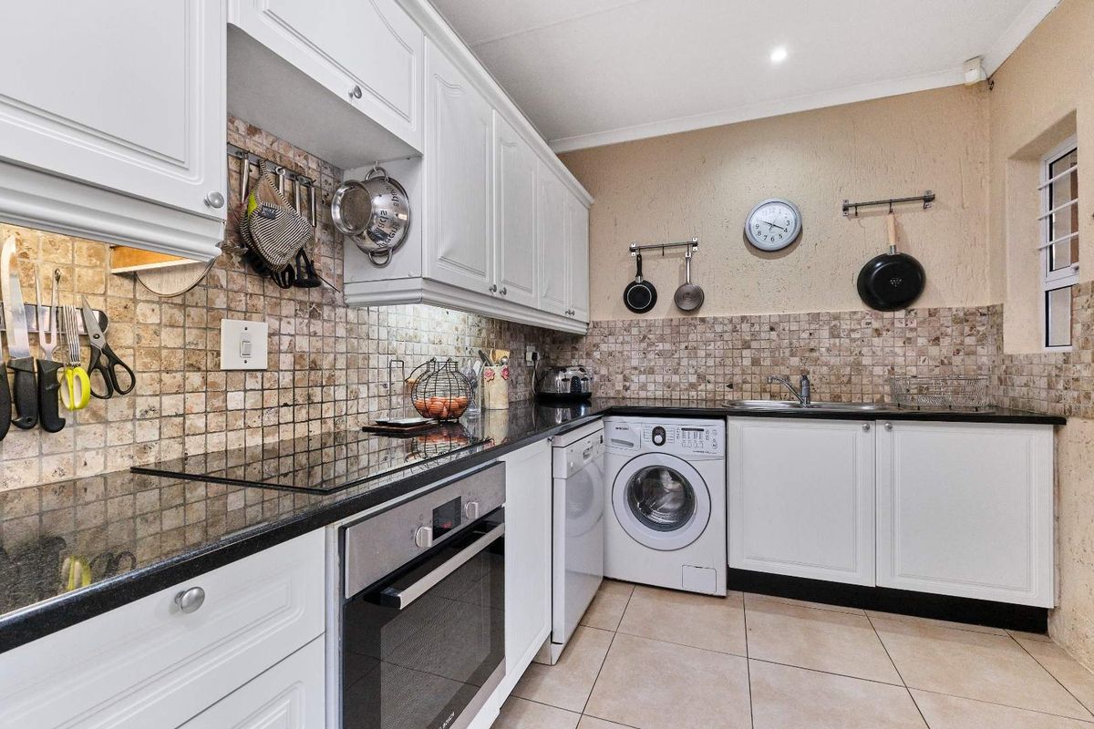 A functional kitchen featuring white cabinetry, granite countertops, a mosaic tile backsplash, built-in oven, and integrated laundry appliance space.