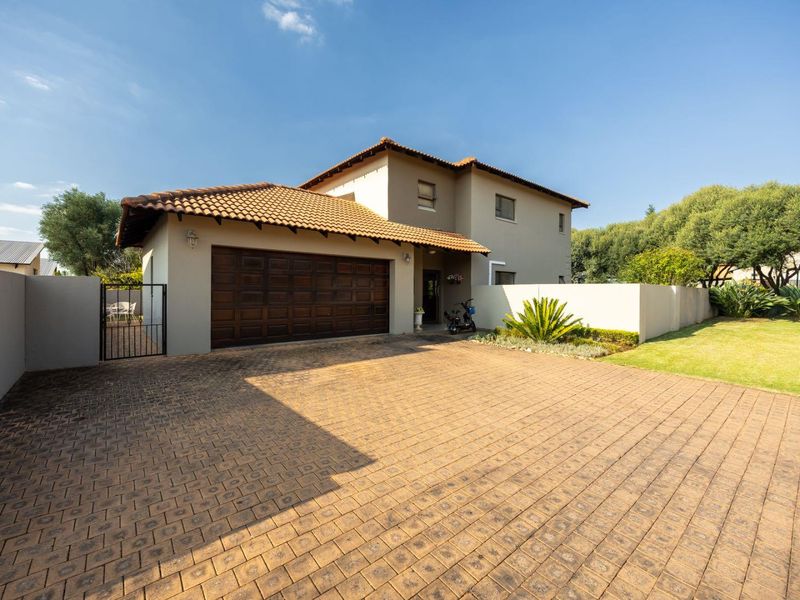 Front view of a double-story house featuring a paved driveway, double garage, and well-maintained garden with boundary walling.