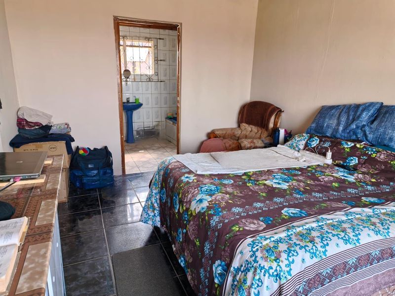 A bedroom featuring dark tiled flooring and direct access to an en-suite bathroom with a pedestal basin.