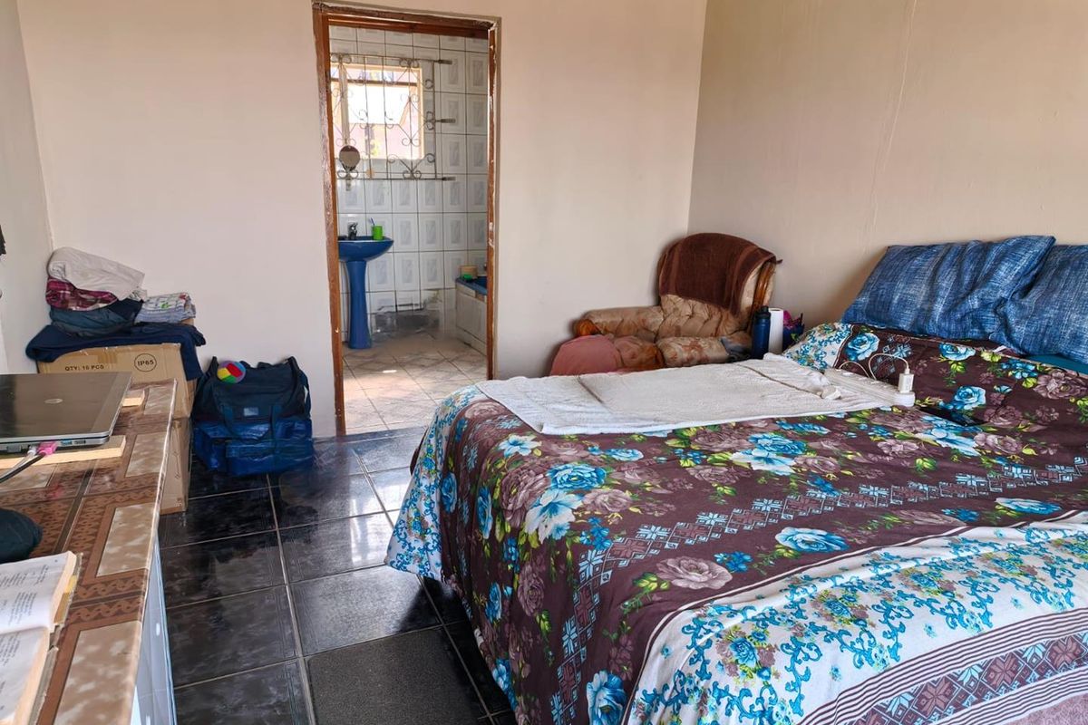 A bedroom featuring dark tiled flooring and direct access to an en-suite bathroom with a pedestal basin.