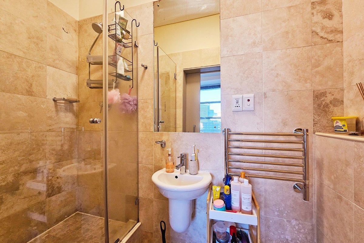 A compact bathroom featuring floor-to-ceiling stone-look tiling, a glass-enclosed shower, a pedestal basin, and a wall-mounted heated towel rail.