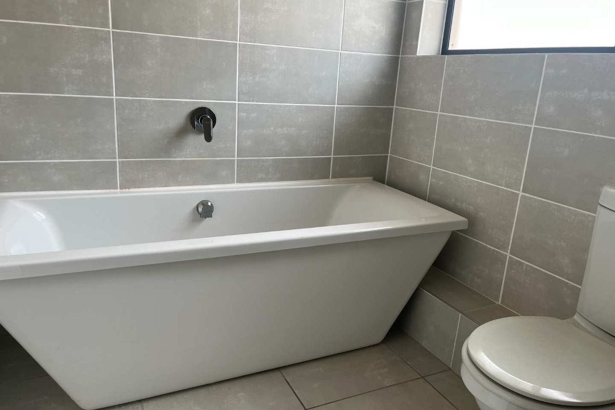 Modern bathroom featuring a sleek freestanding bathtub, wall-mounted mixer tap, and neutral grey wall and floor tiling.