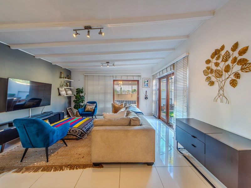 Spacious living room featuring tiled flooring, exposed beam ceilings, and large sliding glass doors that provide ample natural light and access to the outdoors.