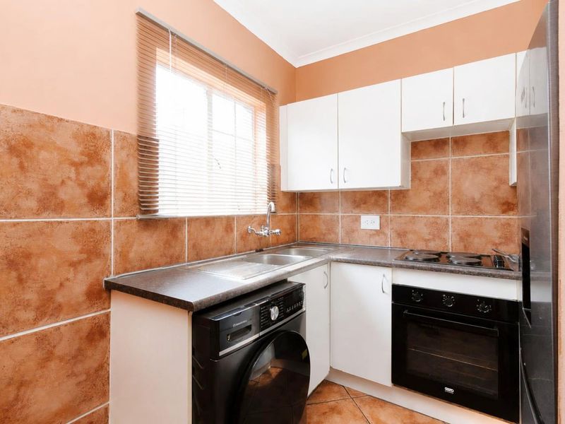 Compact kitchen featuring white cabinetry, dark laminate countertops, tiled backsplash, built-in oven, and electric hob with integrated laundry plumbing.