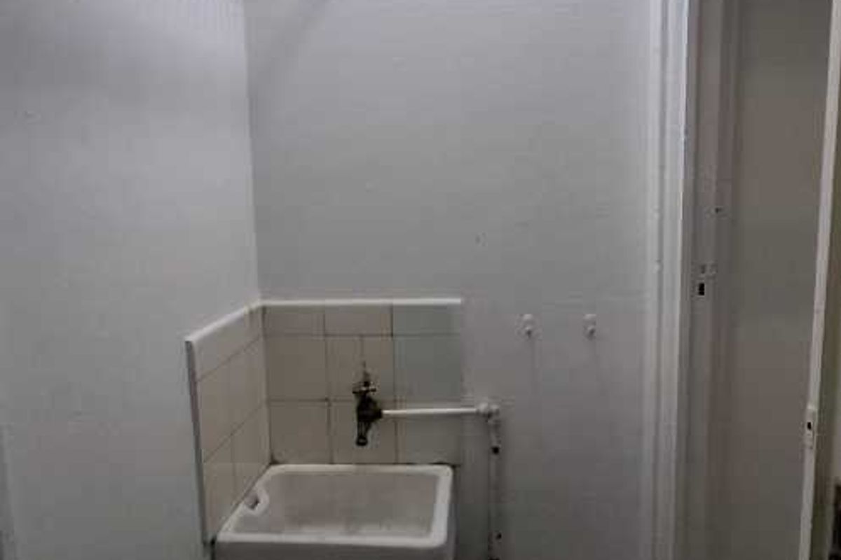 A functional utility or laundry area featuring a wall-mounted sink, exposed plumbing, and overhead wire shelving.