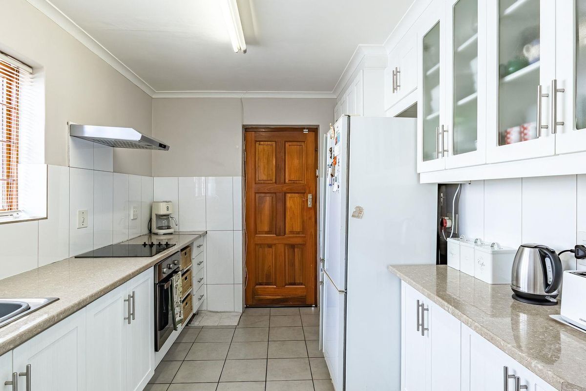 A functional galley-style kitchen featuring white cabinetry, stone-look countertops, a built-in electric hob, extractor fan, and tiled flooring.
