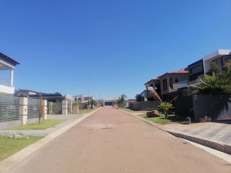 A clear street view of a residential estate featuring paved roads, modern boundary walls, and established residential properties.