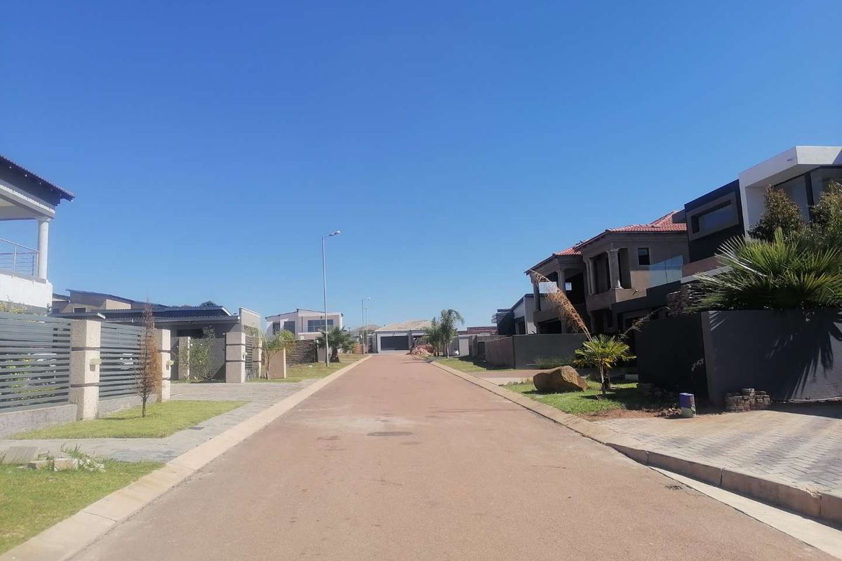 A clear street view of a residential estate featuring paved roads, modern boundary walls, and established residential properties.