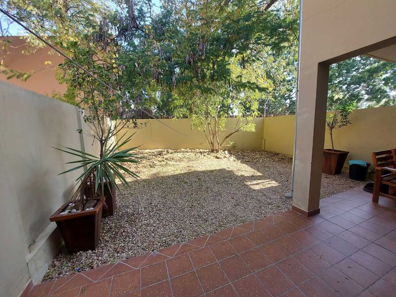 A covered patio area featuring tiled flooring, overlooking a private, low-maintenance gravel garden enclosed by boundary walls.