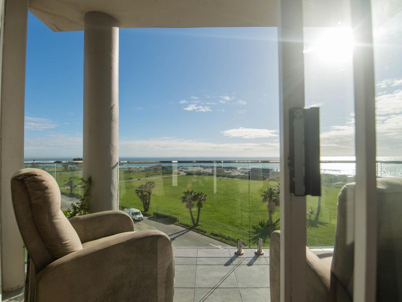 A covered balcony featuring a glass balustrade and tiled flooring, offering expansive coastal and landscape views.