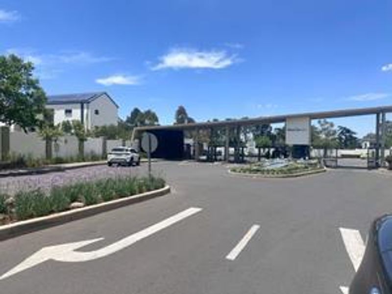 The main entrance and security gatehouse of the townhouse complex, featuring paved access roads and well-maintained landscaped surroundings.