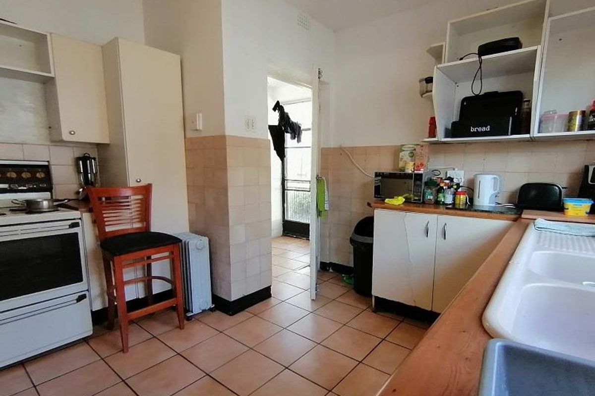 A functional kitchen featuring tiled flooring, built-in cabinetry, a freestanding stove, and a double basin sink, with direct access to an adjacent utility area.