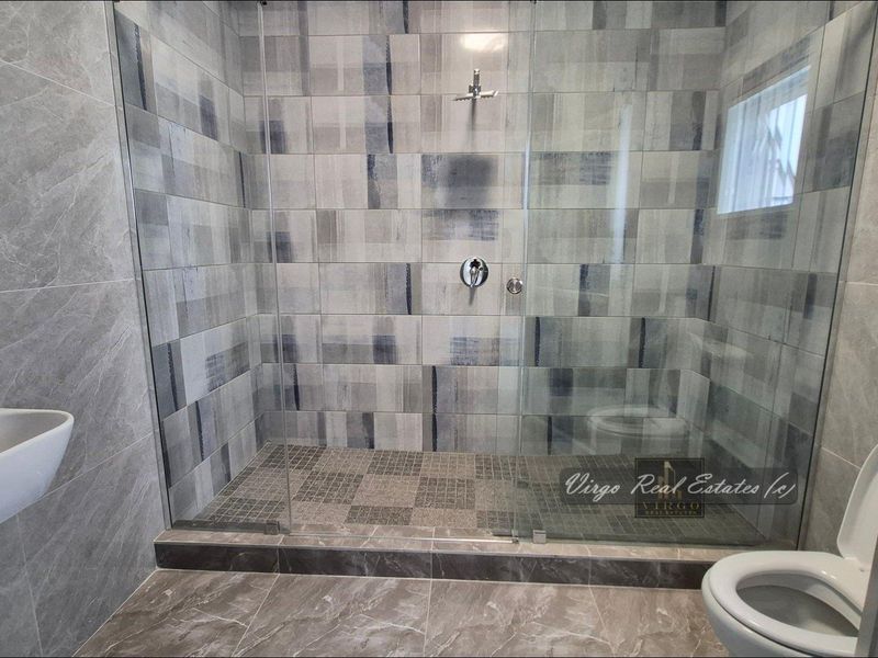 Modern bathroom featuring a spacious walk-in shower with glass enclosure, contemporary wall-hung basin, and stylish patterned wall tiling.