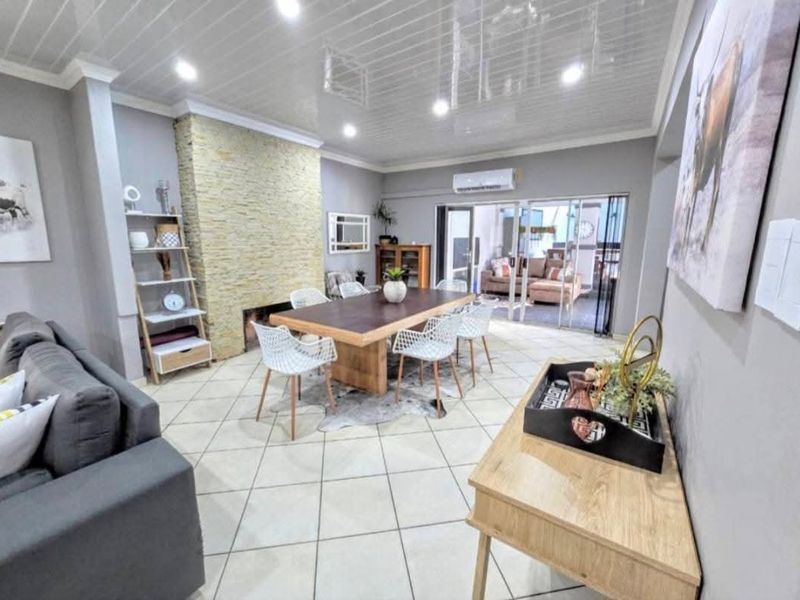 Spacious open-plan living and dining area featuring a stone-clad fireplace, tiled flooring, and direct access to an outdoor patio through sliding glass doors.