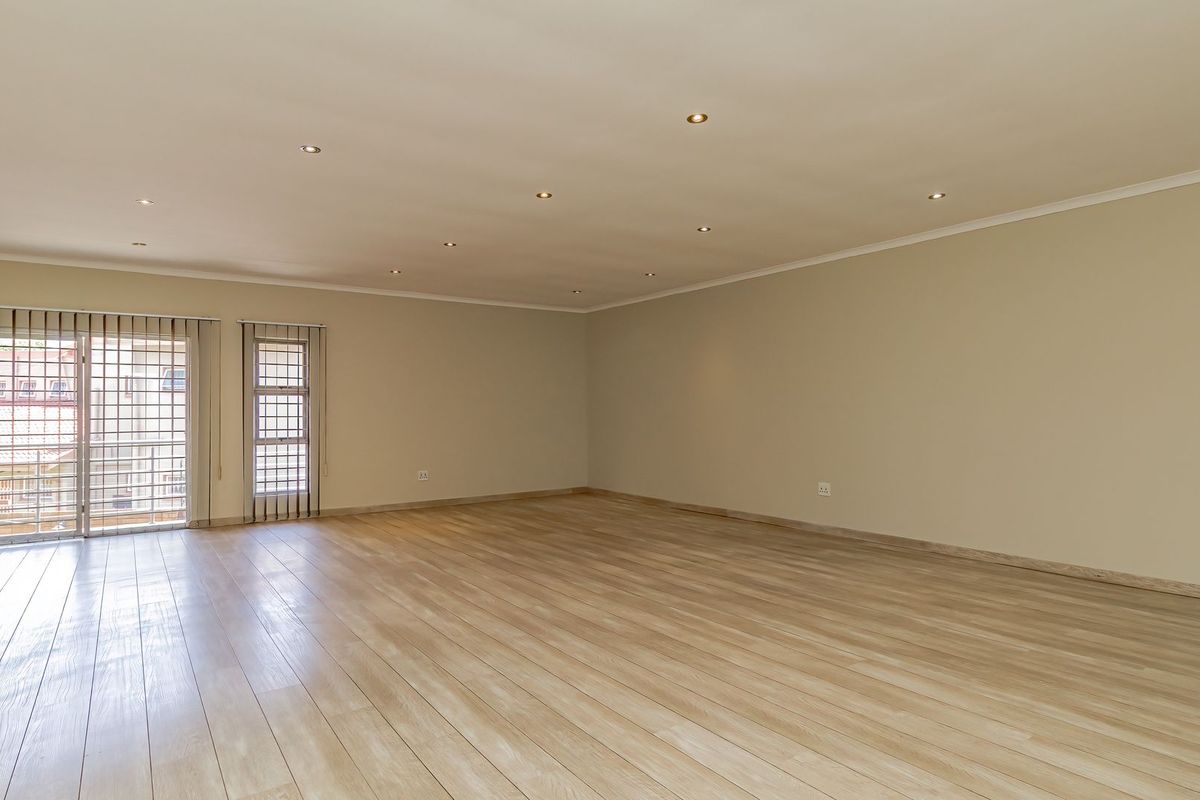 A spacious, empty living area featuring light-toned laminate flooring, recessed downlighting, and a sliding glass door with integrated security gate.