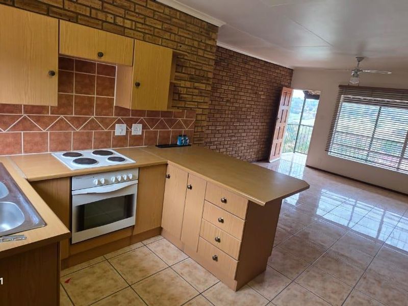 Open-plan kitchen and living area featuring exposed brick walls, tiled flooring, built-in cabinetry, and an electric stove, with direct access to a balcony.
