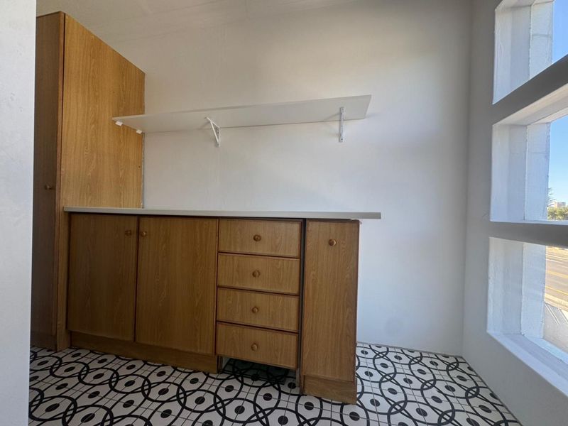 A functional scullery or utility area featuring wood-finish built-in cabinetry, a laminate countertop, wall-mounted shelving, and decorative patterned floor tiles.
